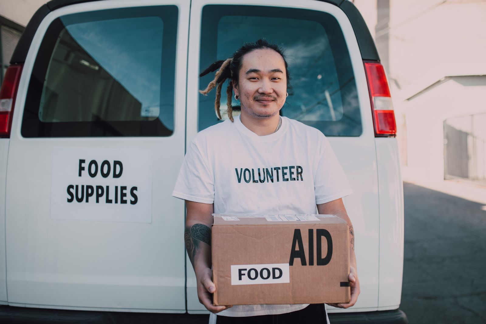 A volunteer holding a box of food supplies beside a community van