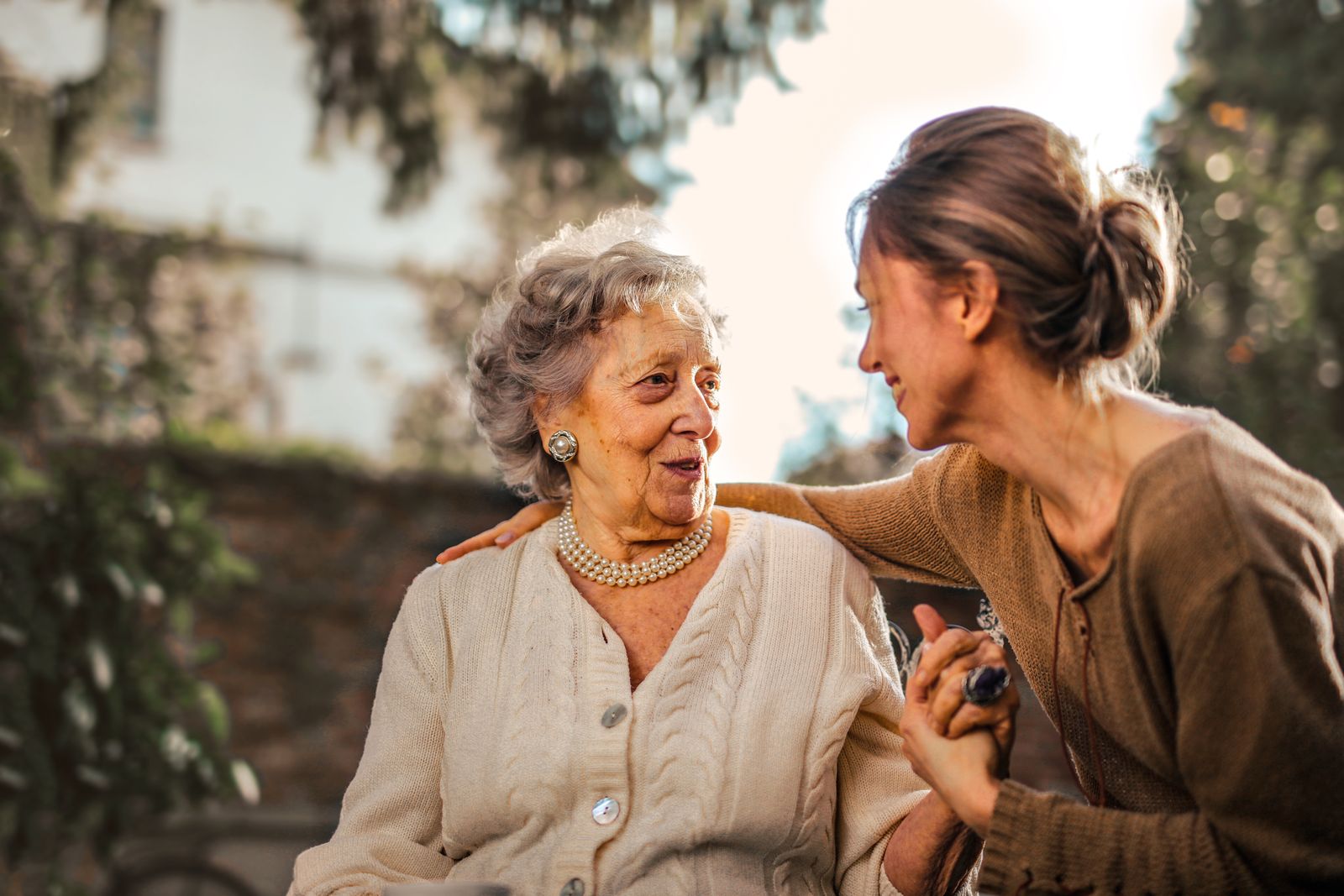 A younger woman sitting with an older woman outdoors, sharing a warm conversation