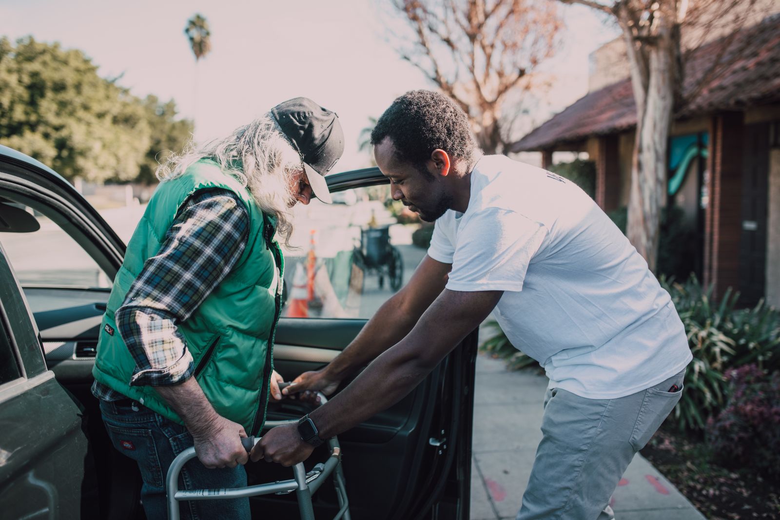 A volunteer helping an older adult with a walker step out of a car