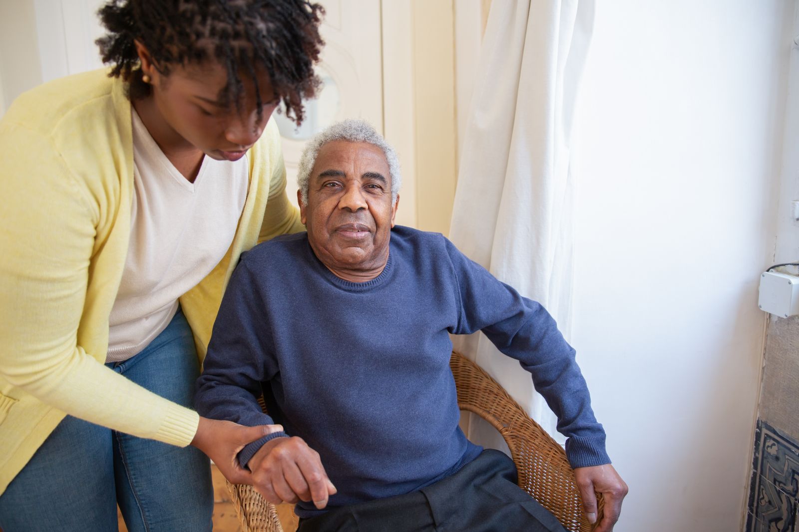 A caregiver standing beside an older man, holding his hand during a home visit